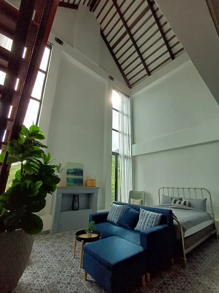 Ground floor of a big villa with a bed, navy sofa, fireplace mantel, and a bright window looking out over the mountains.